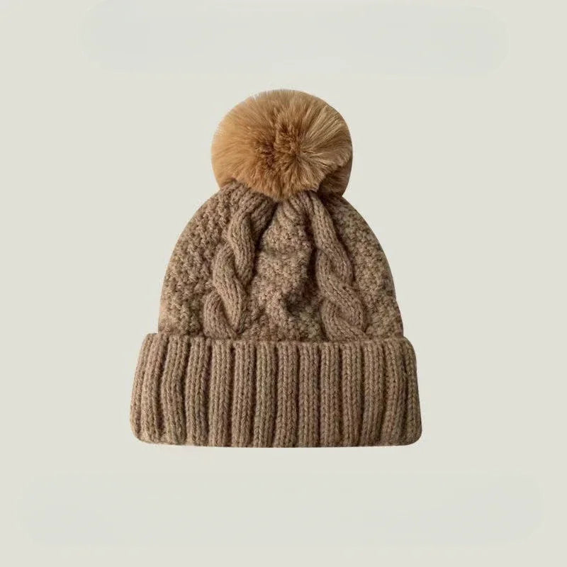 A cosy tan cable-knit beanie featuring a thick ribbed turn-up hem and a matching faux-fur pom-pom on top.