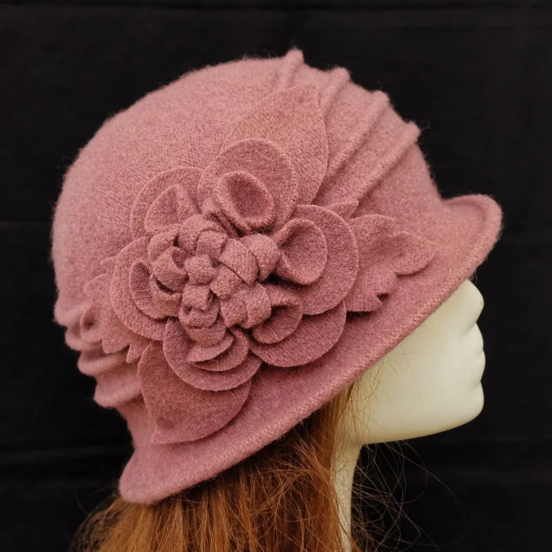 Dusty pink wool felt cloche hat featuring decorative layered flower detailing and side pleats on a mannequin head.