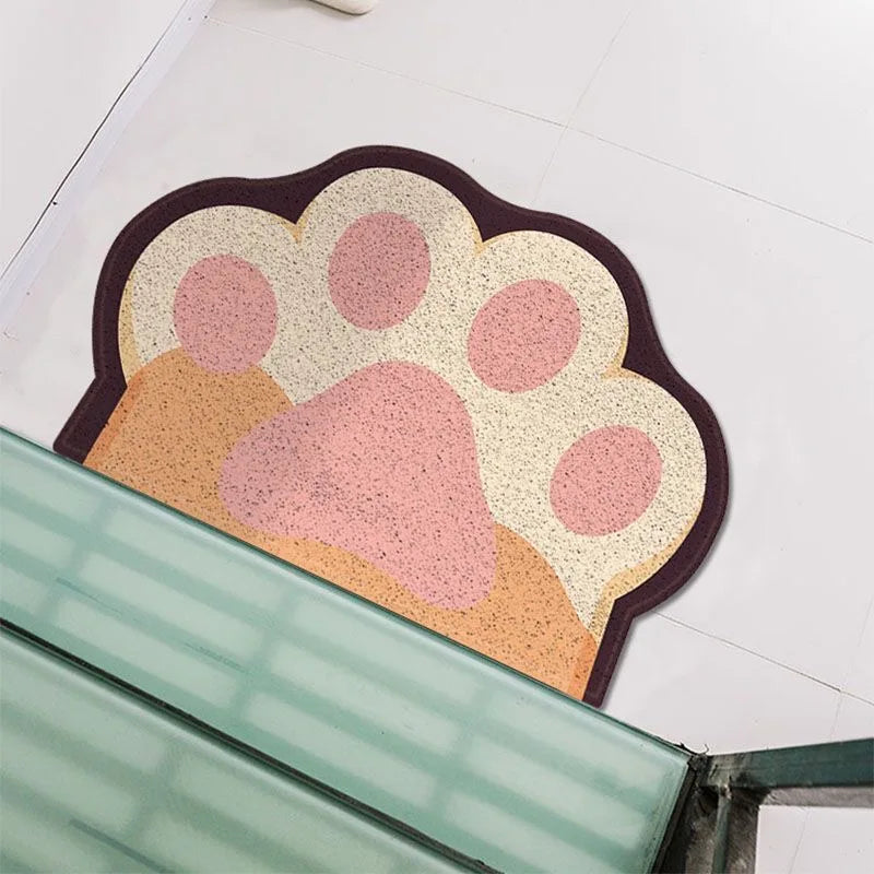 Paw-shaped cat litter trapping mat in cream, pink, and tan with a dark brown border. Textured, non-slip design.