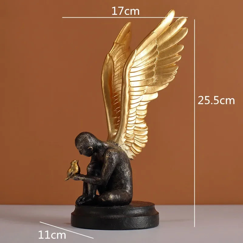 Sculpture of a dark, textured human figure with large gold wings, holding a small gold bird, on a black round base.
