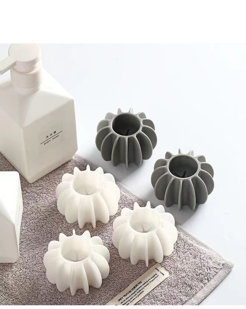 Set of four grey and white silicone, pumpkin-shaped toothbrush holders next to a soap dispenser on a towel.