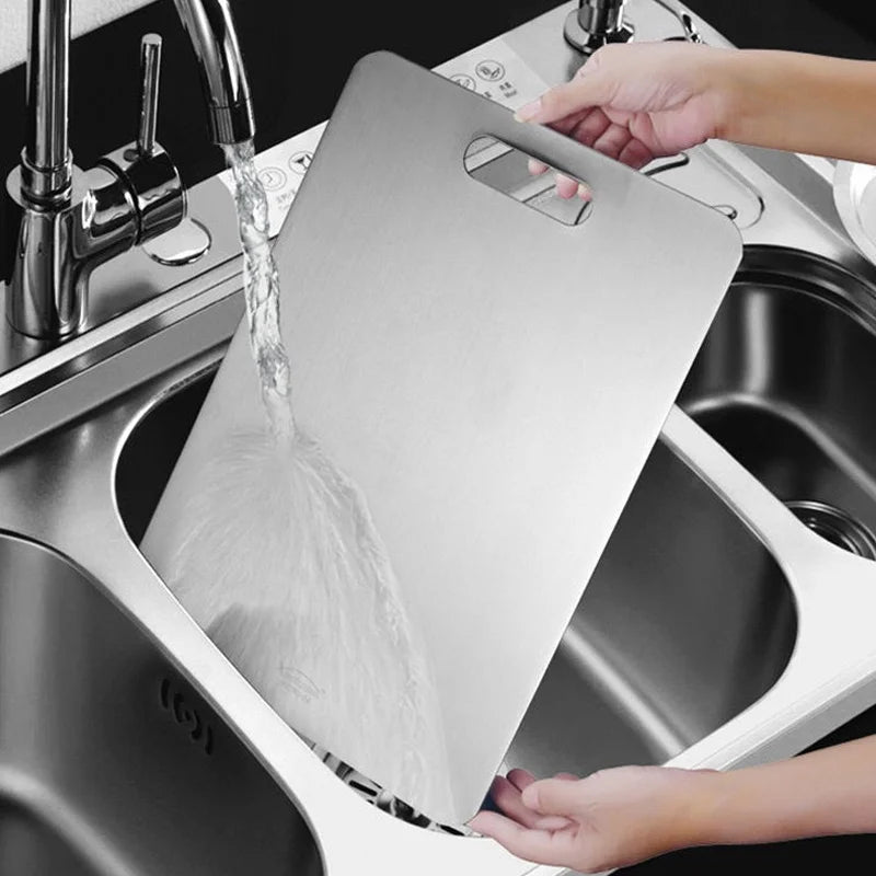 A person rinses a stainless steel cutting board under a kitchen sink faucet.