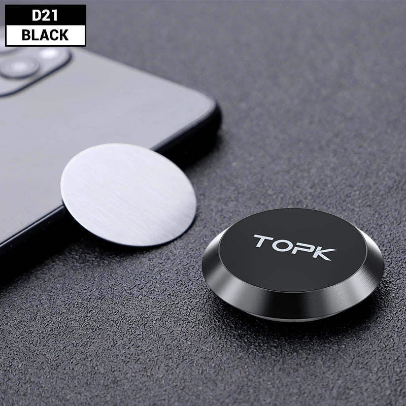 Small, round black magnetic phone holder next to a metal adhesive plate on a grey textured surface.