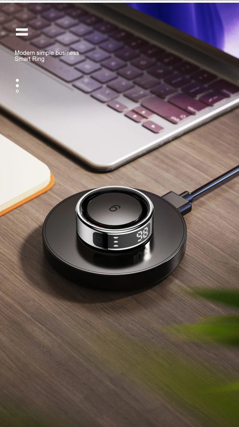 Sleek silver and black smart fitness ring with a digital touch display, resting on a black circular charging dock.