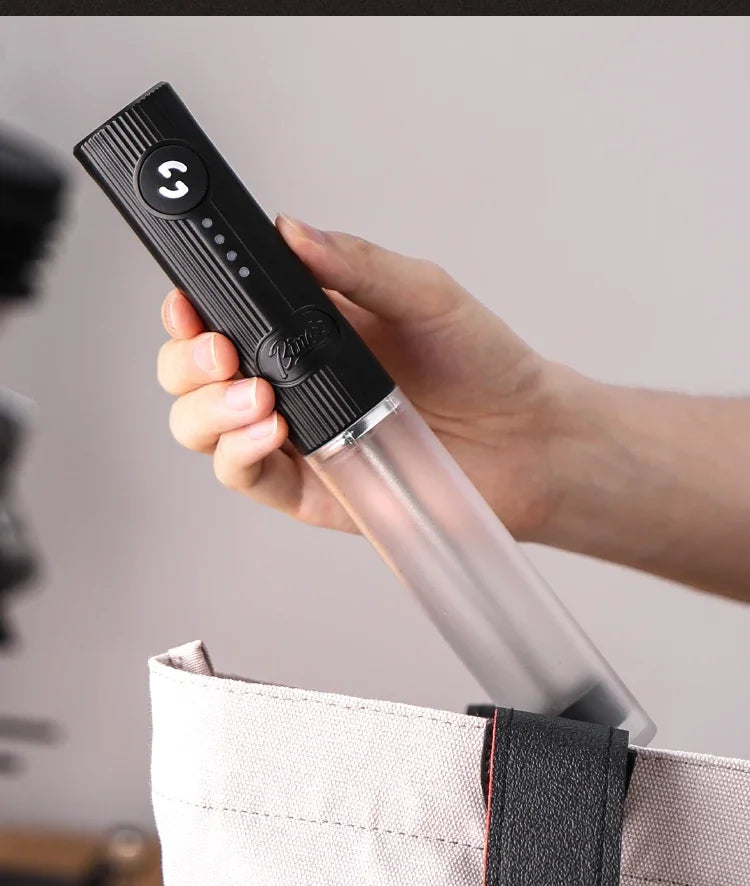 Handheld black electric kitchen whisk with a transparent body, held by a person over a tote bag.