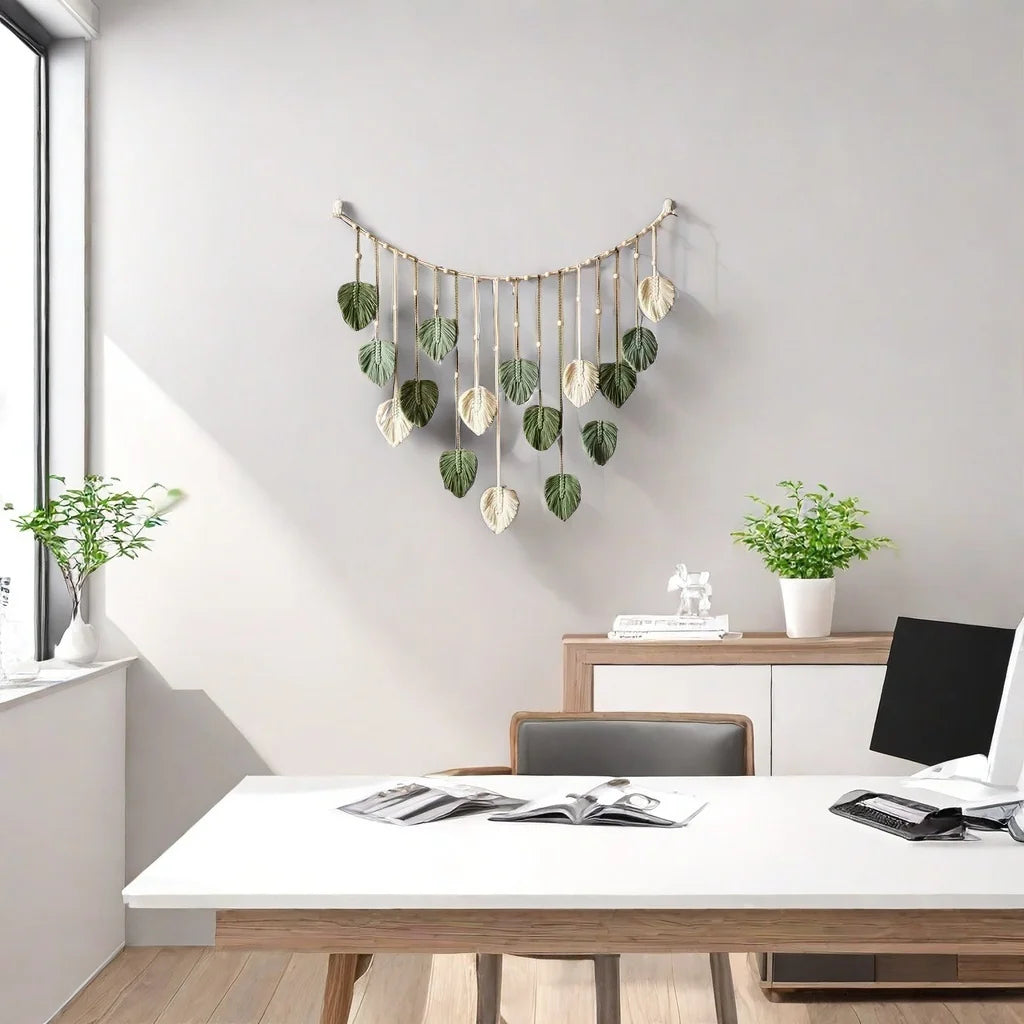 Boho-style wall hanging with sage green and cream macramé leaf tassels suspended from a curved wooden branch.