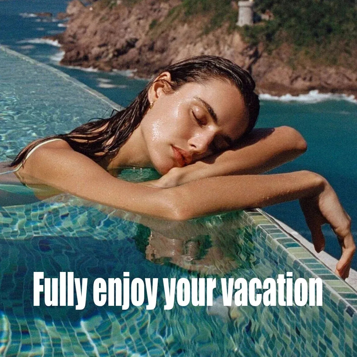 A woman in a light-colored bikini rests her head on the edge of a tiled infinity pool overlooking the ocean.