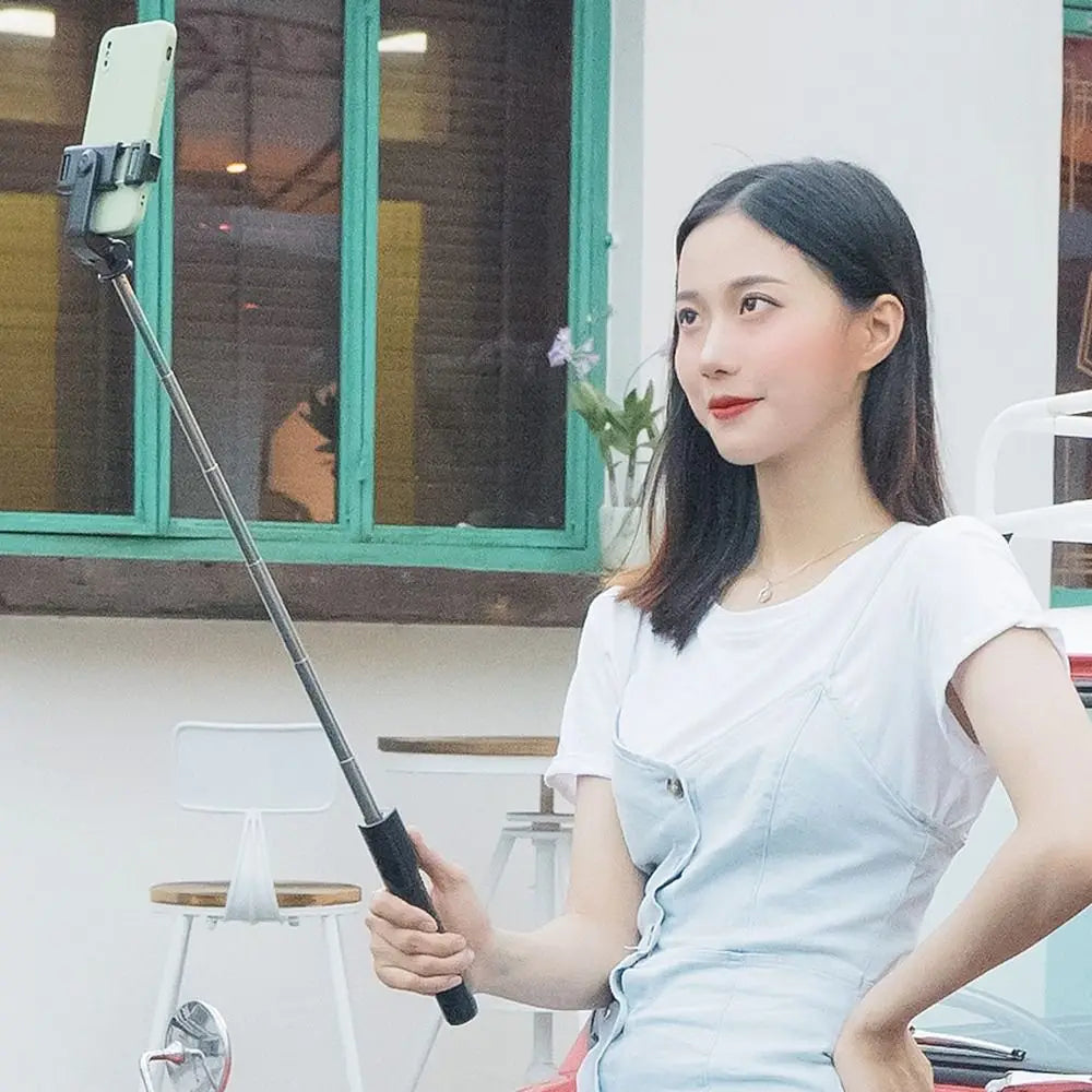 A woman using a black, extendable handheld smartphone selfie stick to take a photo.