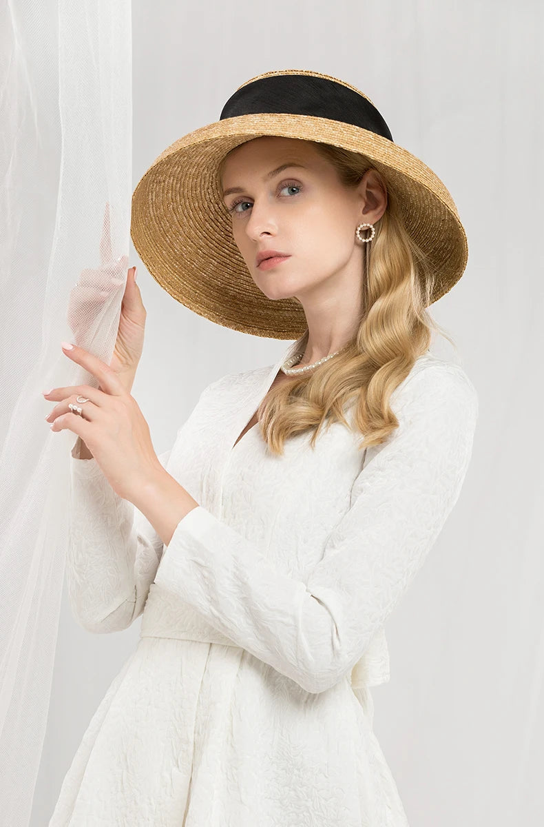 Elegant straw sun hat with a wide brim and a black ribbon band, worn by a woman in a white dress.
