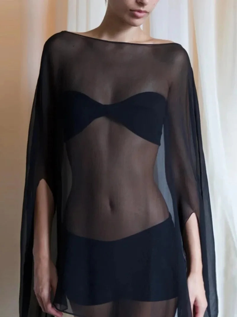A woman wears a sheer black, wide-sleeved, boat-neck top over a simple black bandeau bikini top.