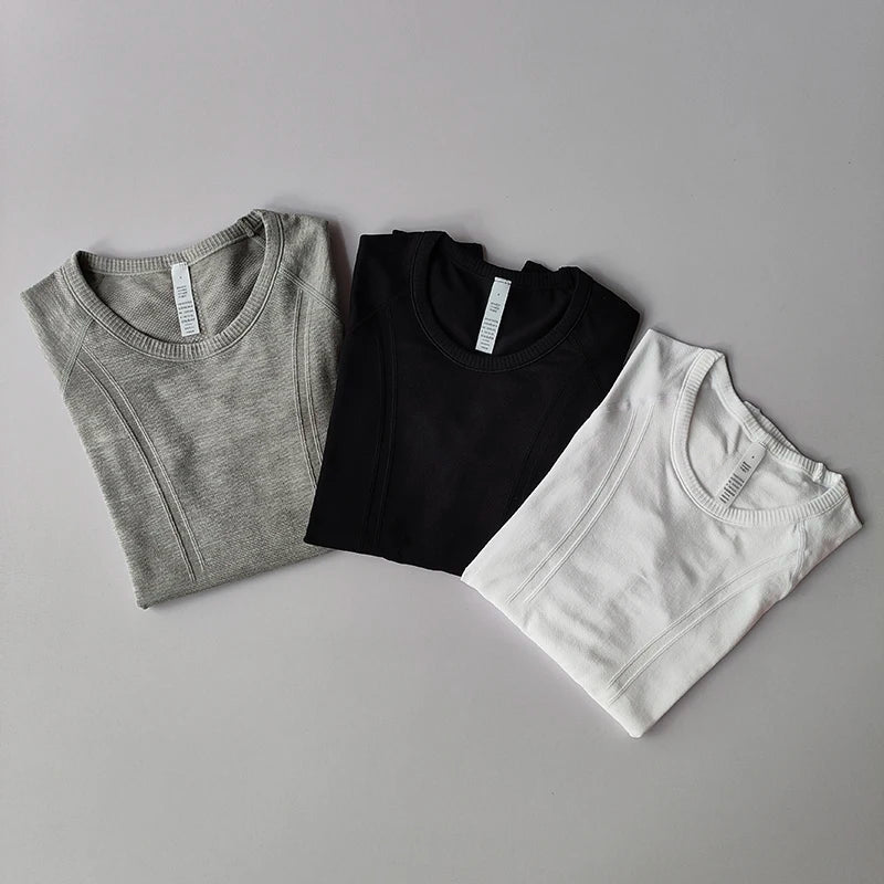 Three folded short-sleeved crew neck athletic tops in grey, black, and white with ribbed texture and side seams.