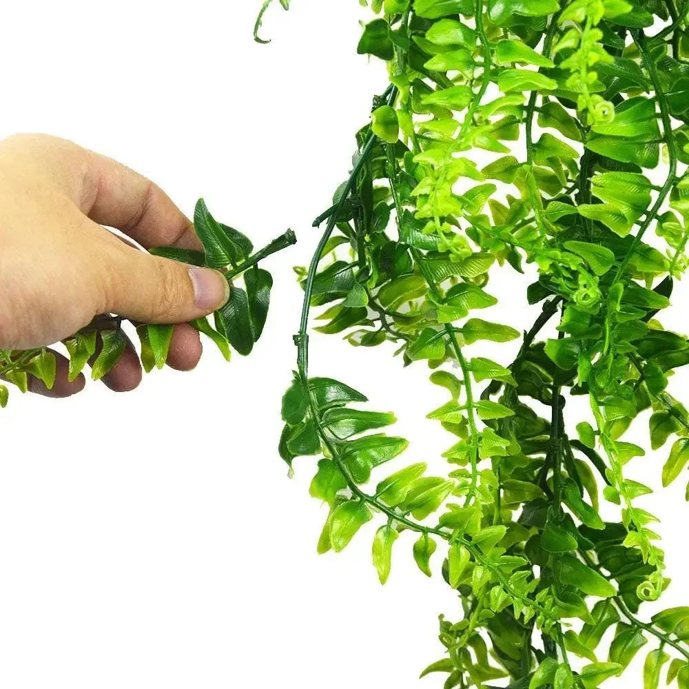 A hand holding a trailing branch of a bright green, artificial plastic Boston fern against a white background.