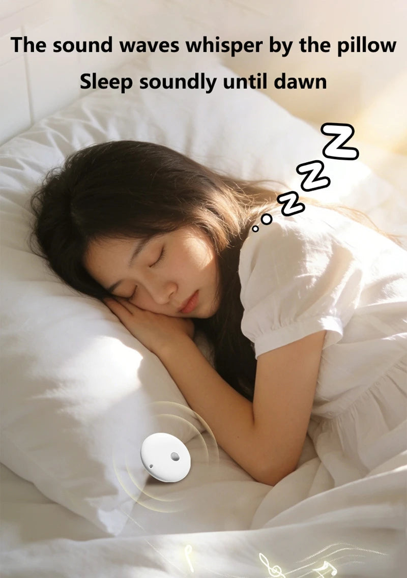 Small white, circular Bluetooth speaker with a suction cup, shown resting on a white pillow next to a sleeping person.