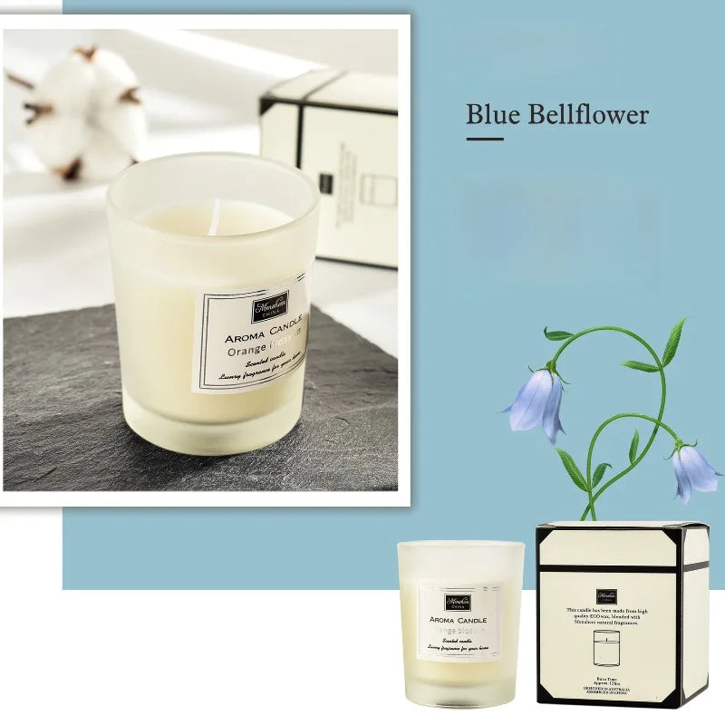 Scented candle in a frosted glass jar with cream wax, presented with decorative blue bellflower and gift box.