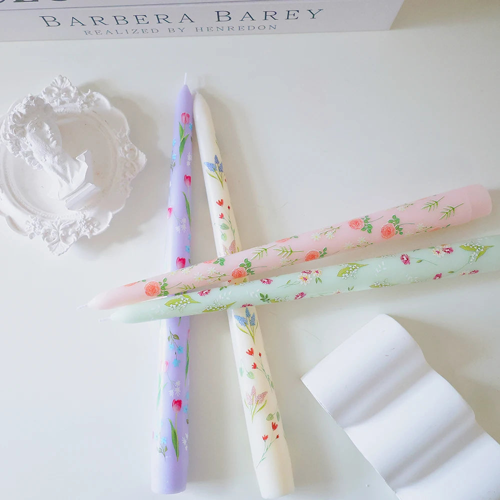 Four elegant taper candles in pastel lilac, cream, pink, and mint, each decorated with delicate floral patterns.