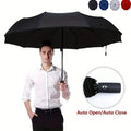 Man holding a large, black, double-layer folding umbrella with auto open-close button.