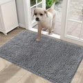 A puppy steps onto a grey, textured, absorbent microfibre doormat placed by a glass door.