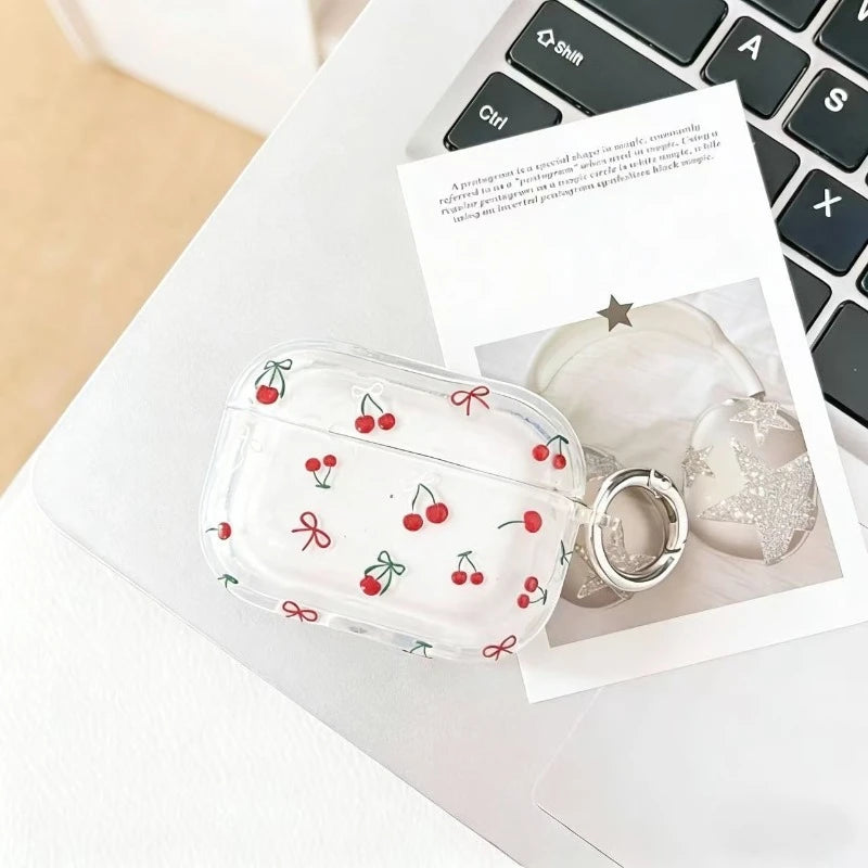 Clear AirPods Pro case with red cherry and bow print, featuring a silver keyring attachment.