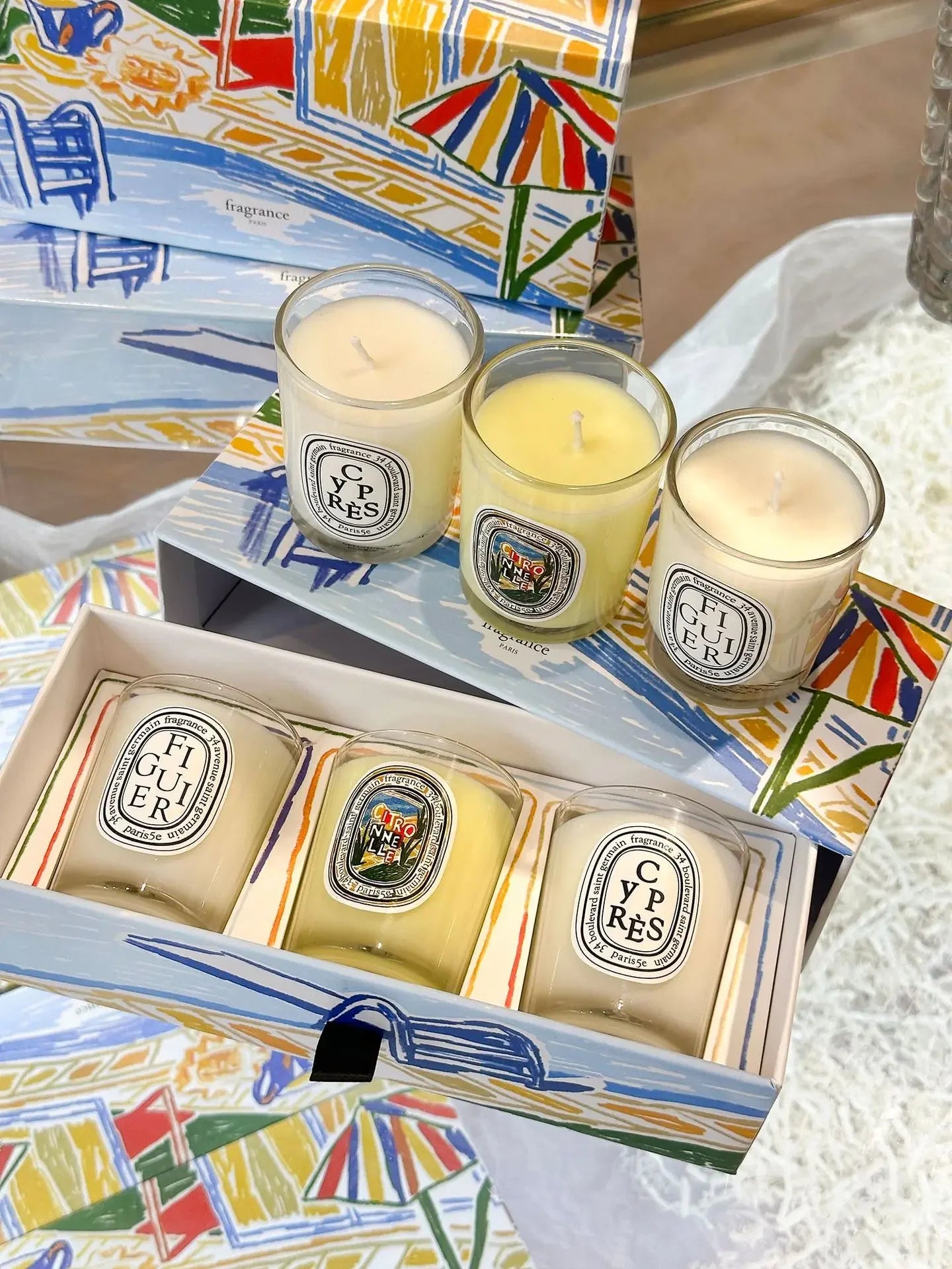 Set of six scented candles in glass votives with illustrative labels, presented in a colourful, artistic gift box.