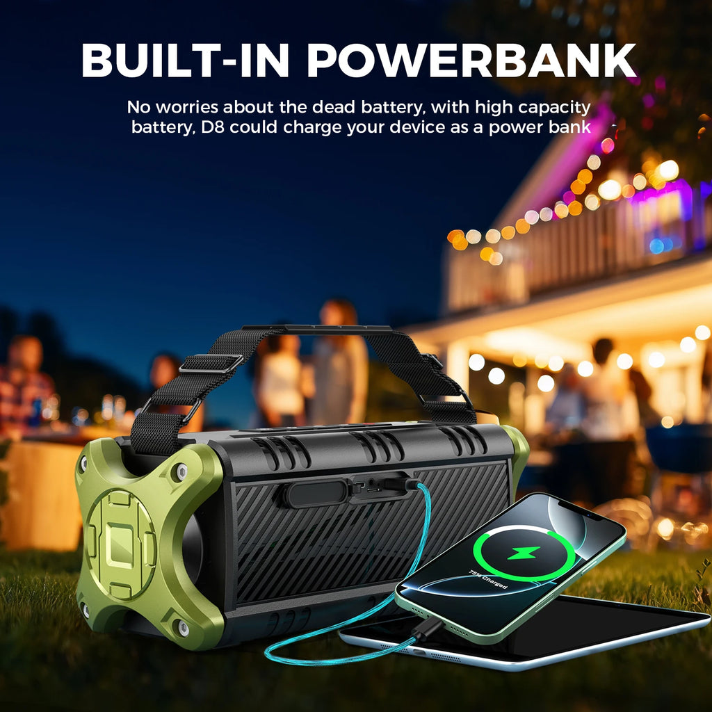 Black and olive green portable wireless speaker with a carry strap, charging a smartphone outdoors at night.