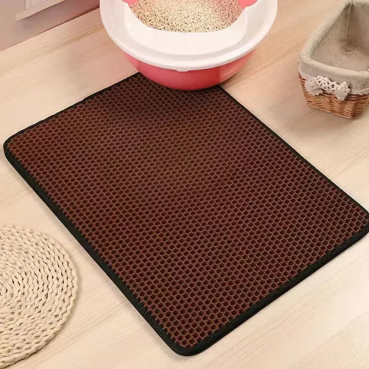 Brown rectangular cat litter mat with a honeycomb texture, featuring a black border on a wooden floor.