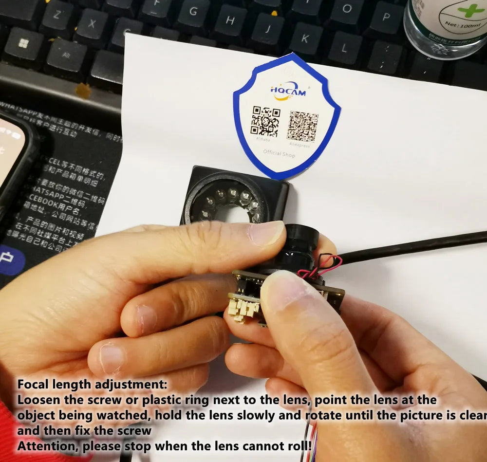Black plastic mini surveillance camera lens component with wired circuit board held by hands.