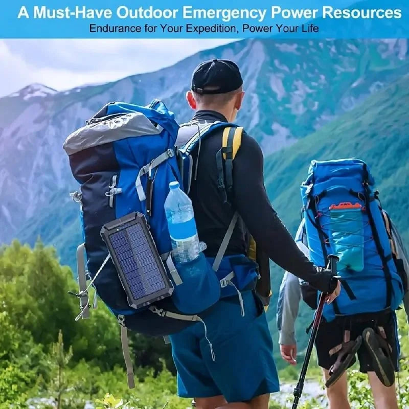 Rugged black solar power bank attached to a hiker’s blue backpack in a mountainous outdoor setting.