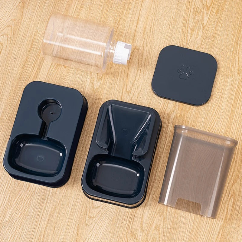 Disassembled navy blue and translucent plastic pet feeder parts, including water bottle and feeding trays, on wood.
