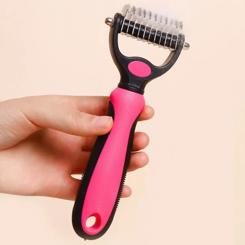 A person holds a pink and black pet grooming rake with metal de-shedding blades, showing loose fur trapped in teeth.