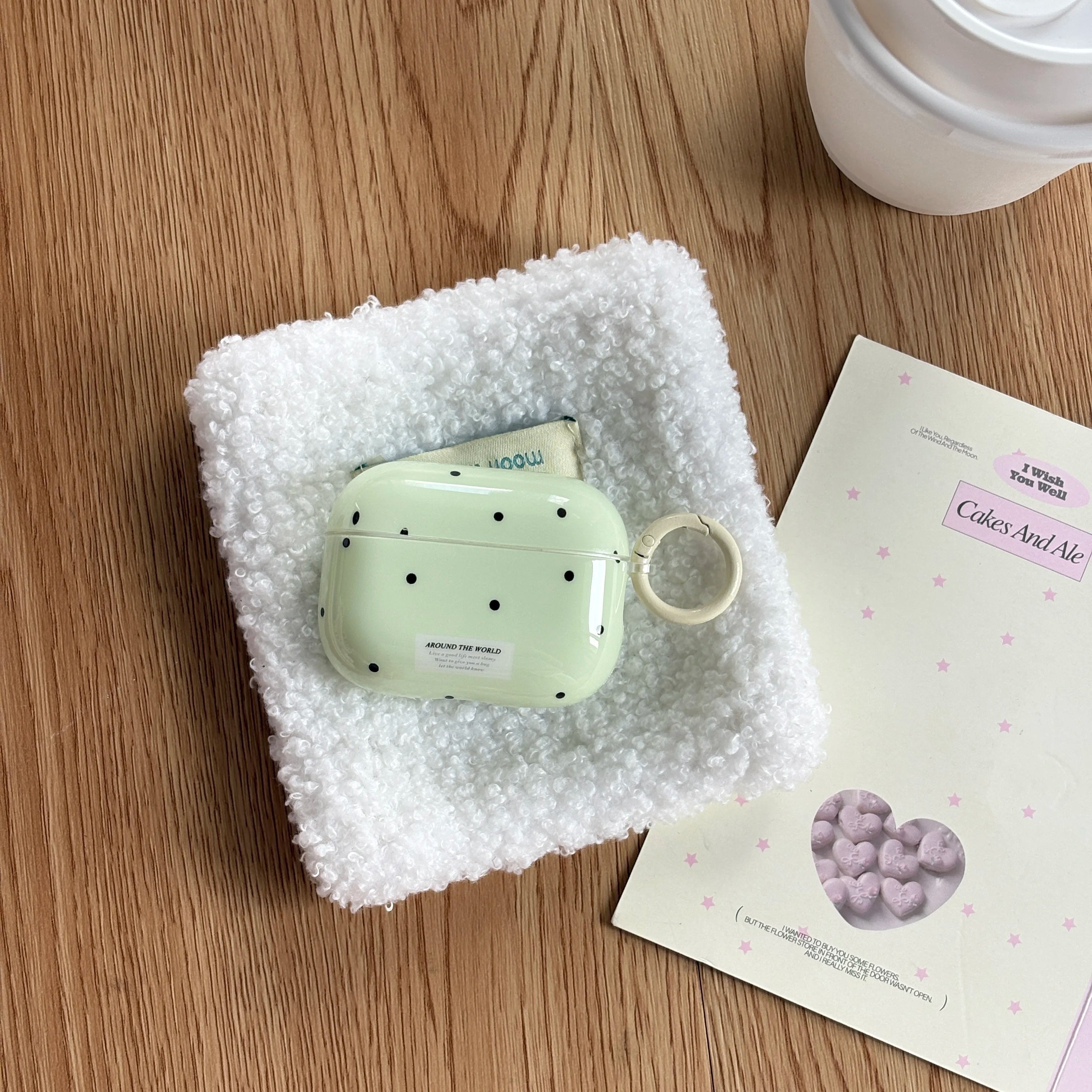 Mint green polka dot hard shell AirPods Pro case with ring attachment, sitting on a white textured fabric square.