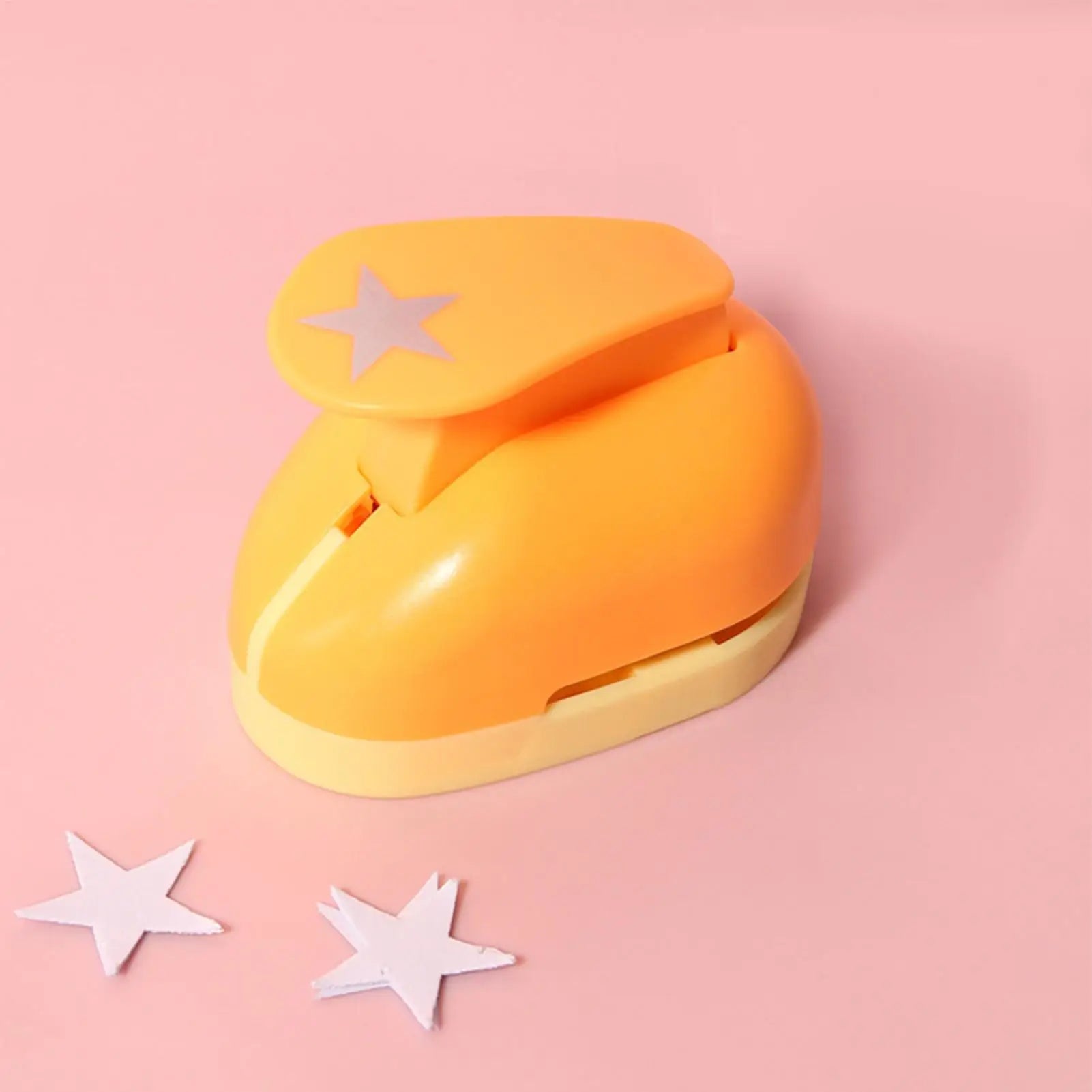 Bright orange star-shaped craft hole punch, sitting on a soft pink background with two white paper stars.