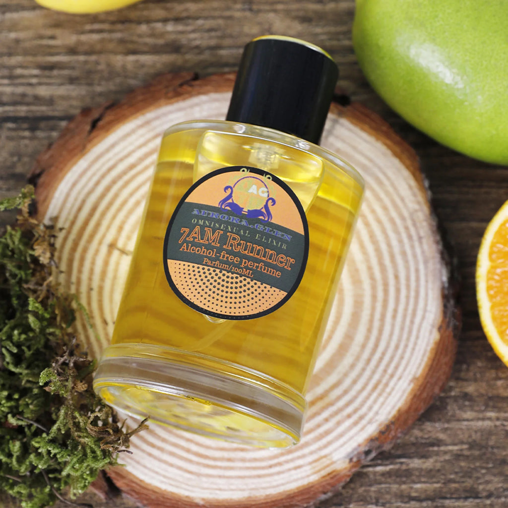 100ml bottle of yellow alcohol-free perfume on a rustic wood slice with fresh fruit and moss.