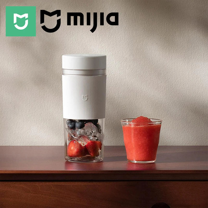 A white, portable, minimalist blender containing strawberries, blueberries, and ice, next to a glass of fruit smoothie.