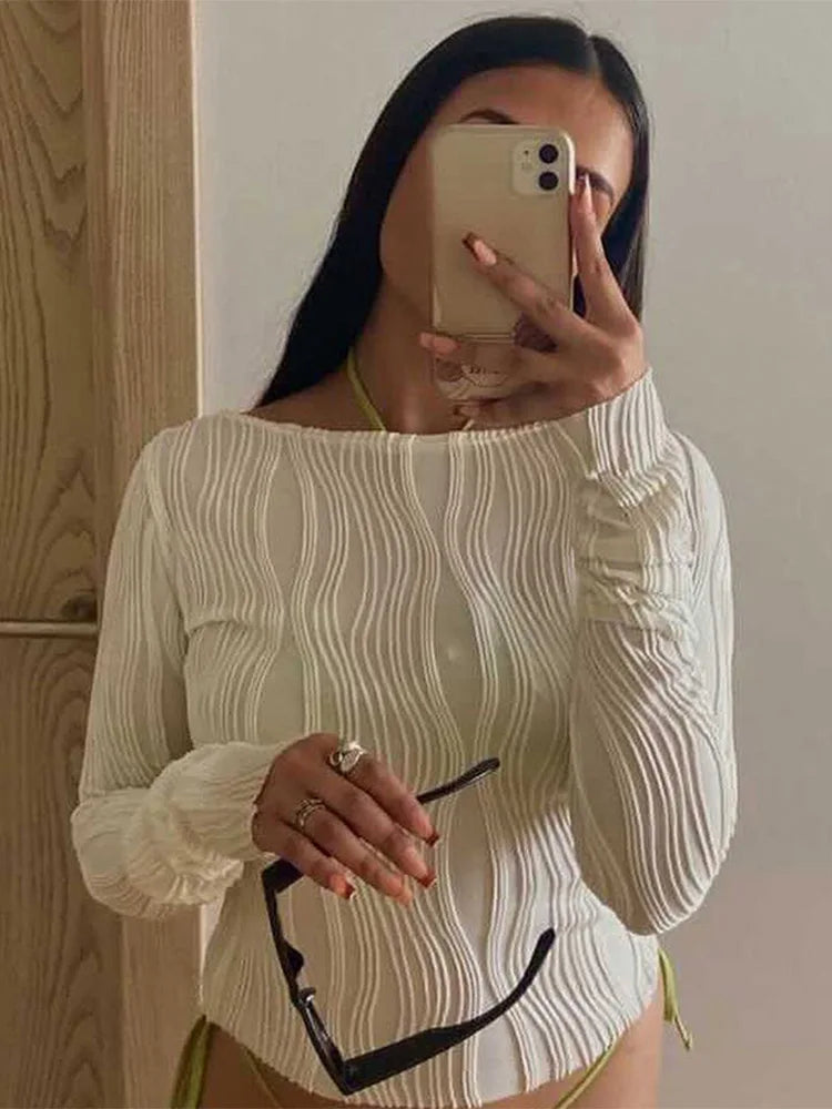 Woman wearing a long-sleeve, white textured ripple-effect top with a round neckline.