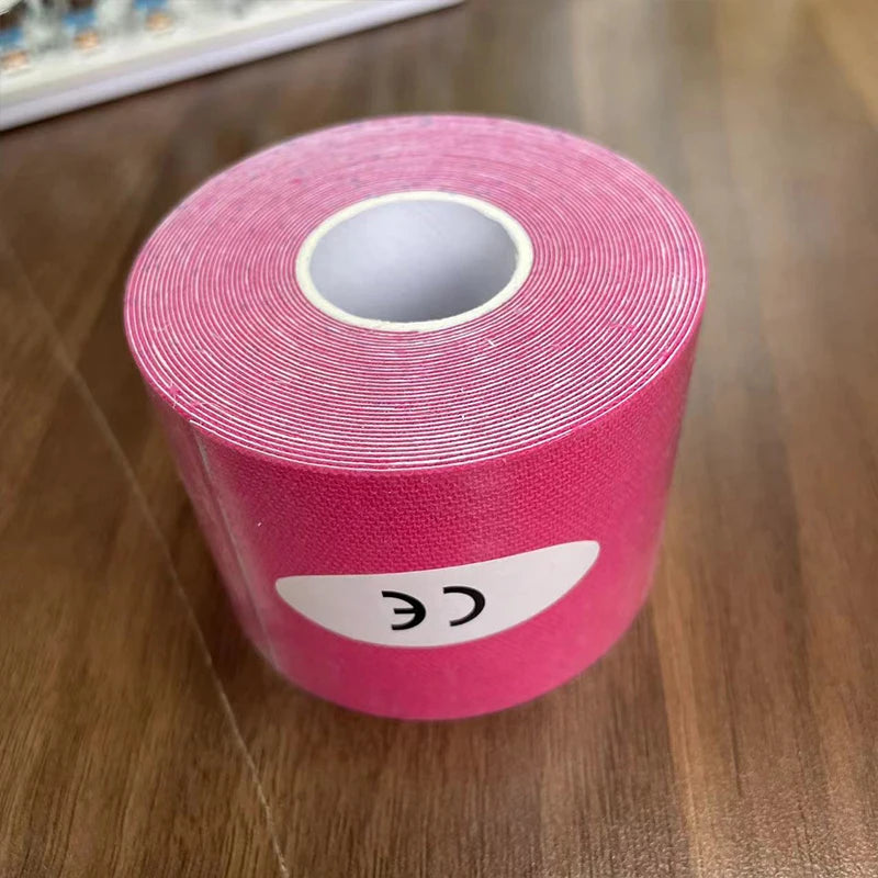 A roll of bright pink kinesiology tape with a white CE sticker on the side, sitting on a wooden surface.