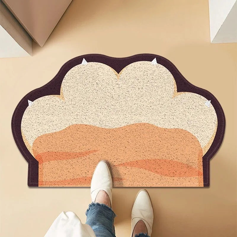 Paw-shaped, anti-slip cat litter mat in beige and orange with a dark brown border. Textured surface traps loose litter.