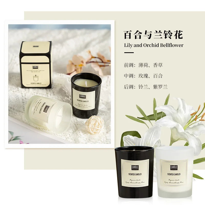 Two luxury scented candles in black and frosted white glass jars, displayed with elegant floral packaging and lily decor.