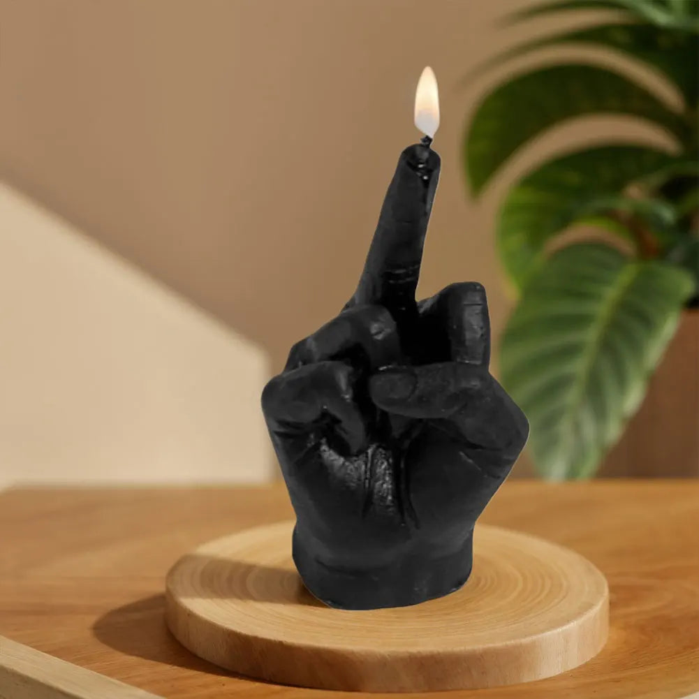 Black candle shaped like a hand giving the middle finger, lit with a single flame, displayed on a wooden base.