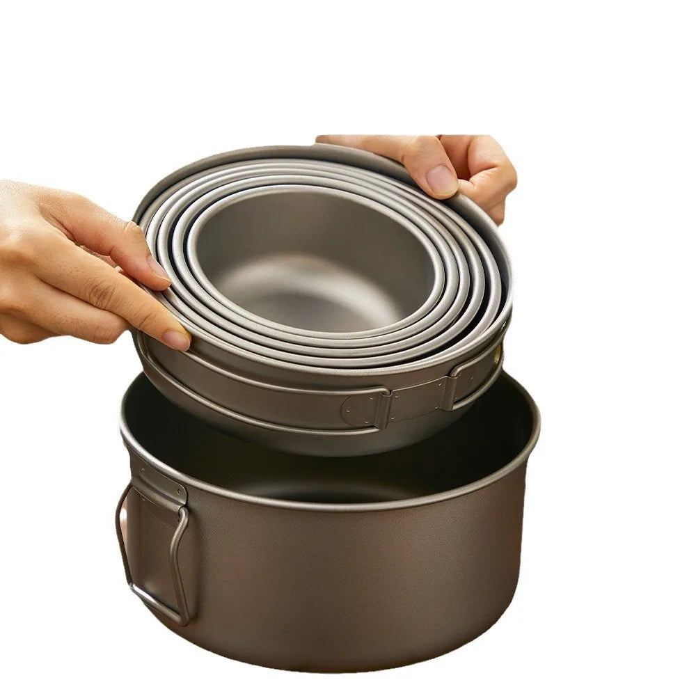 A set of nested, dark-colored metal bowls and a larger pot with foldable handles being held up.