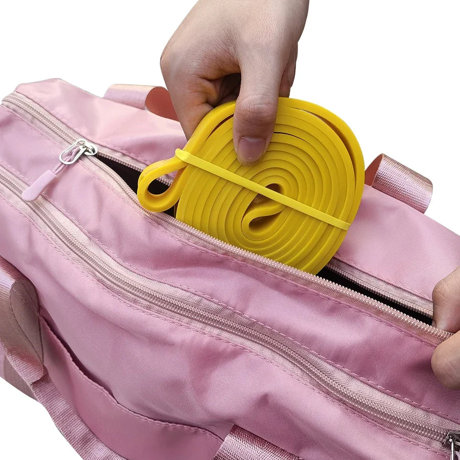 A hand places a coiled yellow resistance band into a pink gym bag.