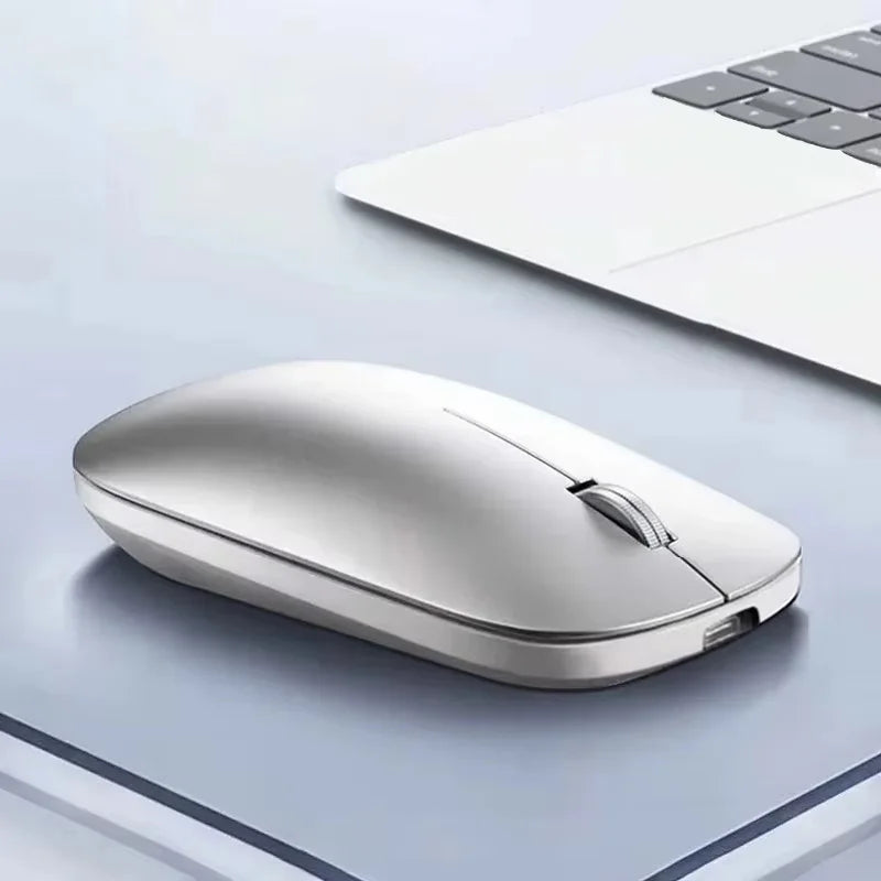A sleek, silver wireless ergonomic mouse with a slim profile and scroll wheel, placed on a desk beside a laptop.