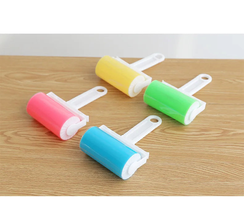 Four lint rollers with white handles and bright yellow, green, pink, and blue adhesive sticky sheets on a wood table.