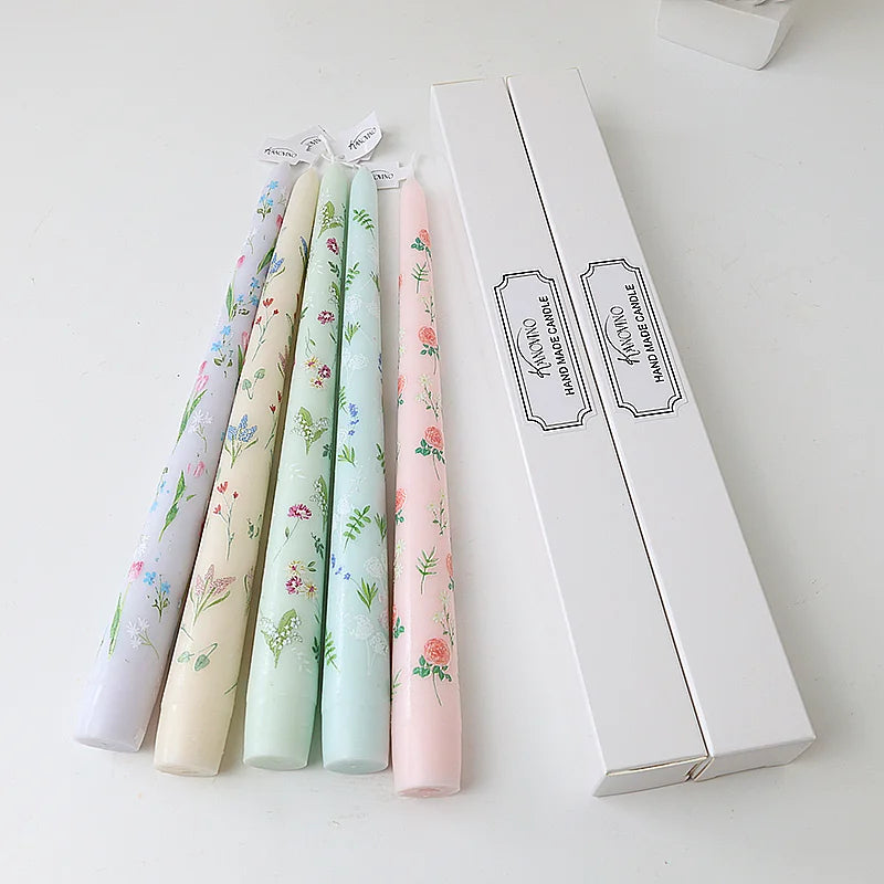 Set of five pastel taper candles featuring delicate botanical and floral prints with two matching white gift boxes.