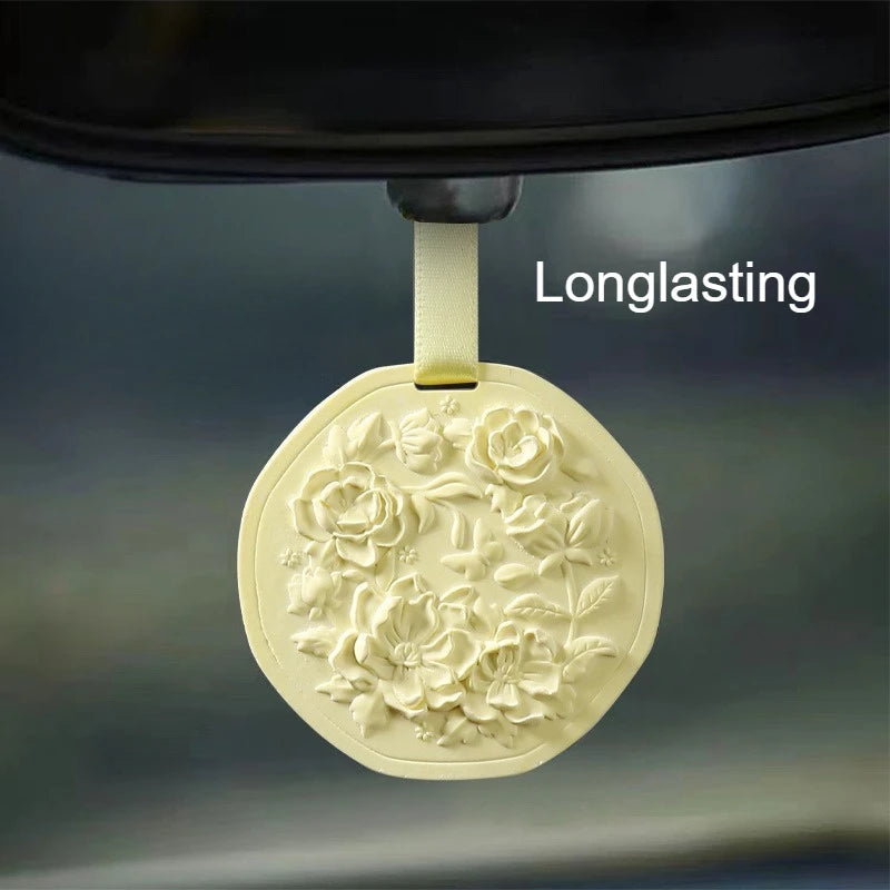 Pale yellow round solid wax fragrance tablet with embossed floral design, hanging by a ribbon.