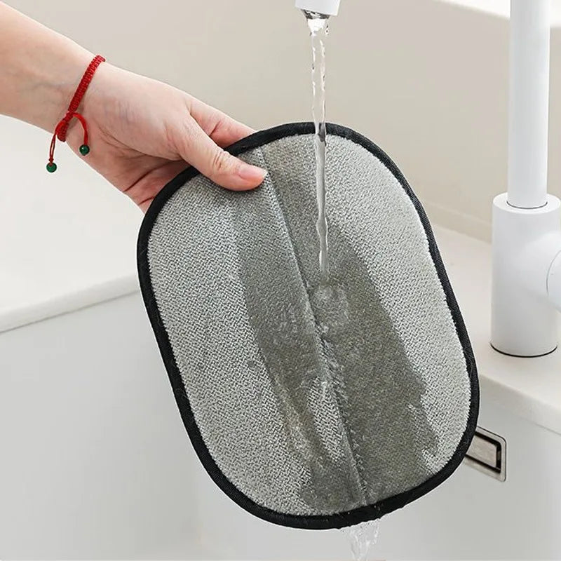 Hand holding a grey, oval-shaped absorbent cleaning pad under a running kitchen tap.