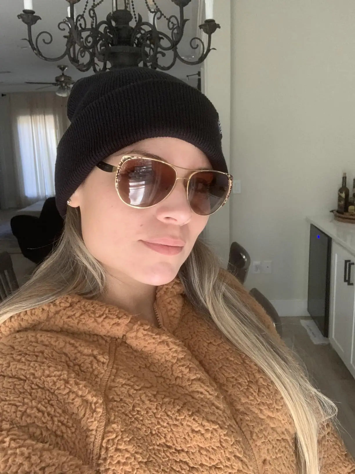 A woman wearing a black knitted beanie hat with a turn-up cuff and brown aviator sunglasses.