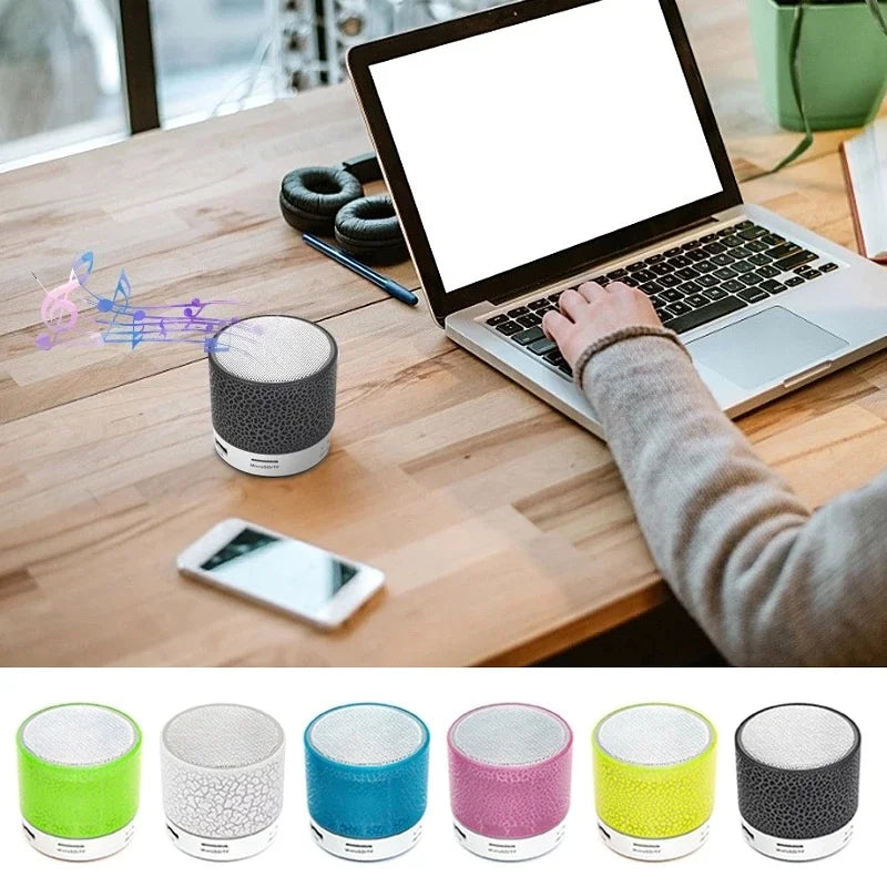 Small, portable Bluetooth speaker with a cracked-pattern design, shown in various colours on a desk.