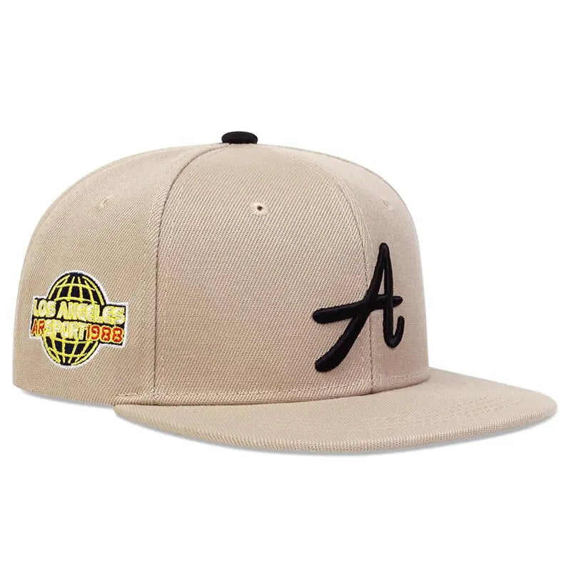 Beige hip-hop baseball cap featuring a black embroidered 'A' and a Los Angeles globe patch on the side.