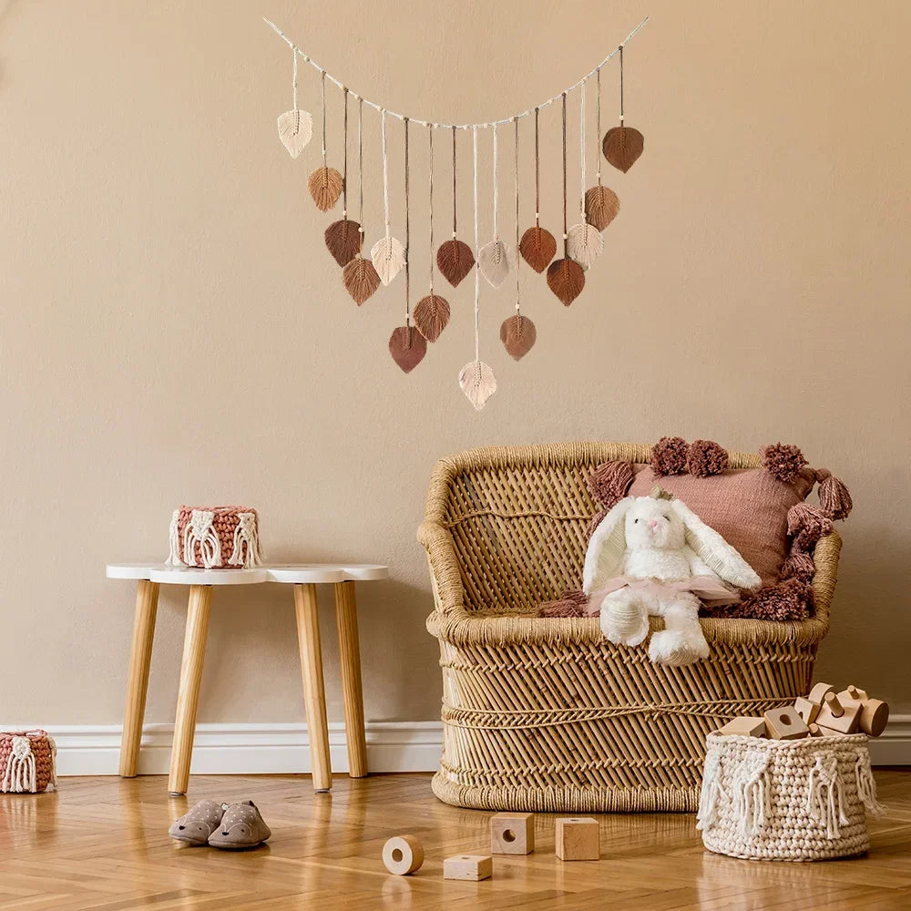 Boho macrame wall hanging featuring hanging leaf-shaped ornaments in neutral and brown shades, displayed in a nursery.