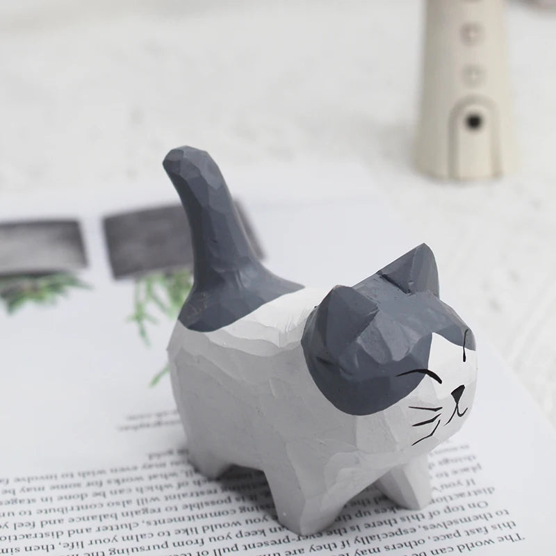 Small, hand-carved wooden cat ornament with grey and white faceted finish, standing on a book.